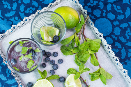 Close up of glass with blueberry mojito cocktail on a metal tray.