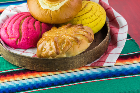 Close up of wooden tray with assorted colorful mexican pastries.