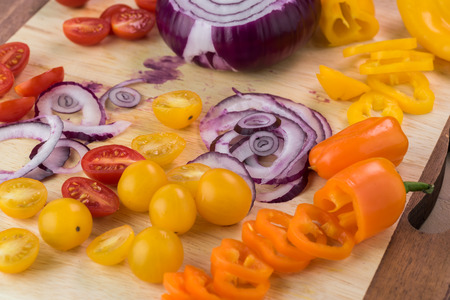 Close up of cutting board with cut vegetables: cherry tomatoes, bell peppers, red onion  - ingredients for salad.の写真素材