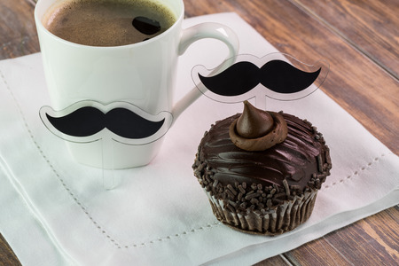 Close up of chocolate cupcake with mustache cupcake topper and cup of coffee.の写真素材