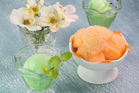 Close up of ice cream bowls with lime and orange sherbet on a blue wooden background.の写真素材