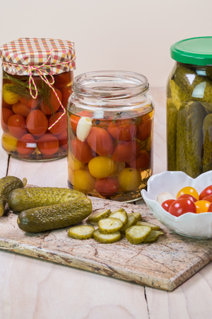 Close up of  pickled vegetables in glass jars and pickles on a cutting board.の写真素材