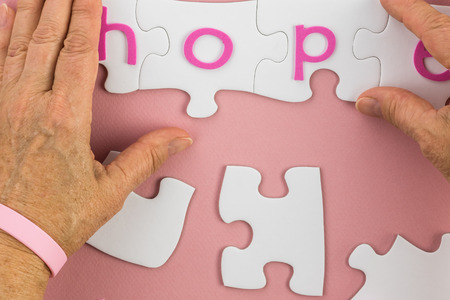 Female hands putting pieces of a puzzle to complete the word for hope on pink background.の写真素材