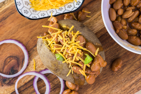 Close up of  loaded baked potato with  beans on a cutting board.の写真素材
