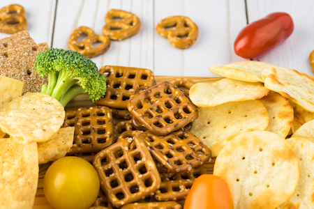 Close up of of cutting board with variety of snacks. Chips, crackers, pretzels.