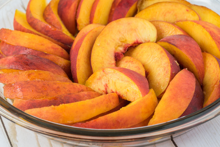 Close up of cut peaches - ingredient for homemade peach cobbler in baking dish.