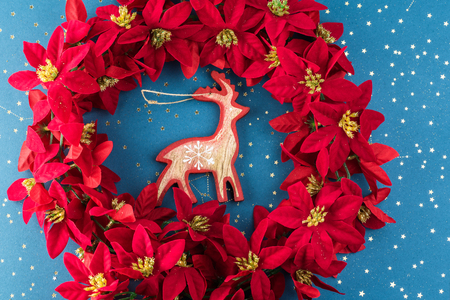 Top view of Christmas wreath with poinsettia flowers  and wooden deer on a blue background.の写真素材