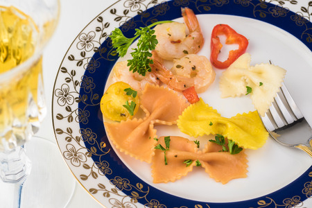 Close up of plate with  shrimp veggie colorful bowtie pasta and glass of wine on wooden background.の写真素材