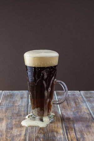 Close up of glass of dark beer. Beer foaming over the top of the mug.の写真素材