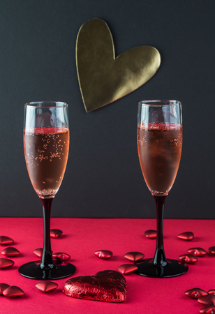 Glasses of sparkling wine on a red and black background decorated with symbol heart pieces.の写真素材