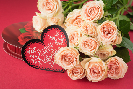 Close up of pink roses and candy heart shaped box for Valentines Day on a red background. Greeting card concept.の写真素材
