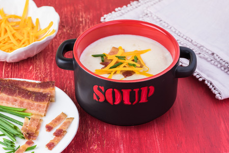 Bowl with cauliflower soup and ingredients for load: cooked bacon, cheddar cheese and chives.の写真素材