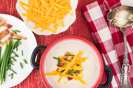 Bowl with cauliflower soup and ingredients for load: cooked bacon, cheddar cheese and chives.