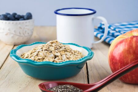 Close up of bowl with oats, chia seeds, milk, blueberries and apple - ingredients for overnight oats with chia seeds, blueberries and apple.の写真素材