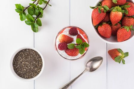 Top view of glass with chia pudding with stawberry sauce and berries, chia seed in bowl and strawberris.の写真素材