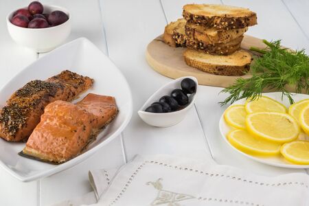 Close up of smoke roasted salmon, black olives, toasted bread, sliced lemon, fresh  dill - ingredients for smoke roasted salmon sandwich.の写真素材