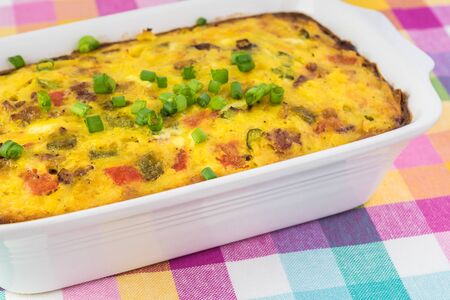 Close up of dish with breakfast casserole with bacon, bell peppers and jalapeno,, potatoes, cheese.