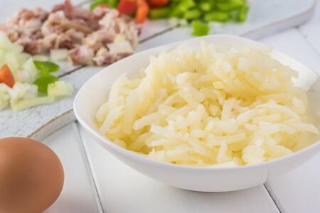 Close up of ingredients for breakfast casserole: shredded frozen potatoes, cut bacon, bell pepper...