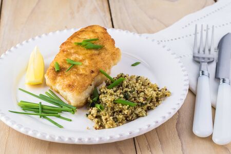 Close up of fried piece of cod fish and mediterranean style quinoa on a white plate.の写真素材
