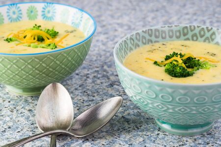 Two bowls with homemade  broccoli cheddar cheese on a kitchen table.の写真素材