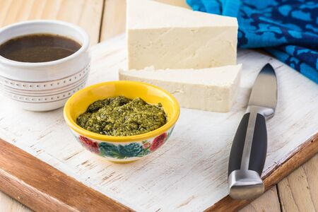 Cooking. Organic firm tofu, basil pesto, balsamic vinegar on cutting board.