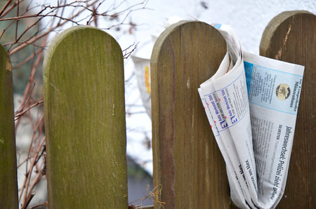 Delivery of a folded newspaper clamped between pickets of a wooden garden fence in Berlin, Germany - January 13 2018のeditorial素材
