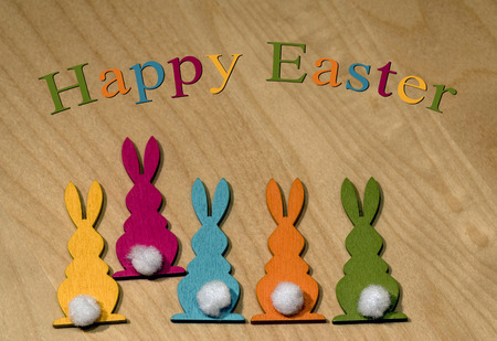 Five colorful wooden Easter bunnies in a row and one of them is dancing out of line - Easter greetings in Englishの写真素材