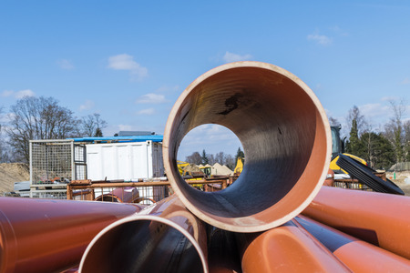 Looking through a large plastic pipe on a construction site with material, containers and...
