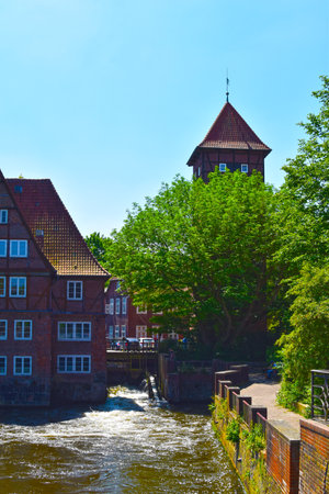 Lueneburg, Germany - June 5, 2018: View on the river Ilmenau in the German medieval town of Lueneburg. You can see a medieval tower and a weir under trees.のeditorial素材