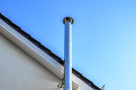 Stainless steel chimney and parts of a roof in front of a bright blue sky.