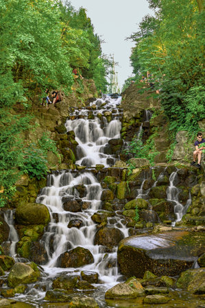 Berlin, Germany - June 28, 2019: Waterfall in the Victoria Park in Berlin, Kreuzberg. Young people sit on the edge of the watercourse to refresh themselves in the heat of the day.のeditorial素材