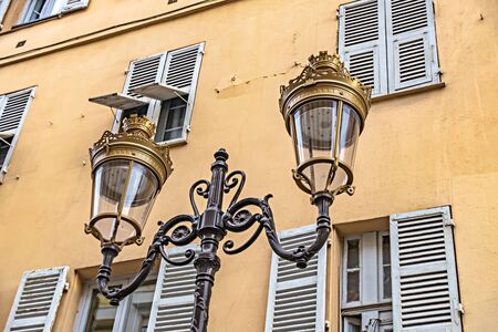 Historic two-armed street lamp in Nice, France, in front of a house facade with wooden shutters.の写真素材