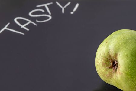 A pear on a black cutting board with the inscription Tasty. The focus is on the pear in foreground on the right side.の写真素材