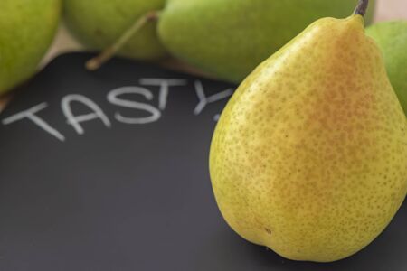 Some pears on a table behind a black cutting board with the inscription Tasty. The focus is on the pear in foreground on the right side.の写真素材