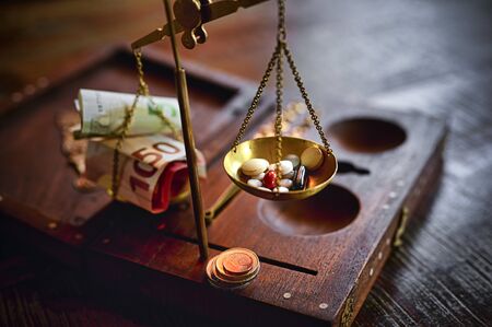 An old scale with money on one side and tablets on the other as a symbol of healthcare costs. The...