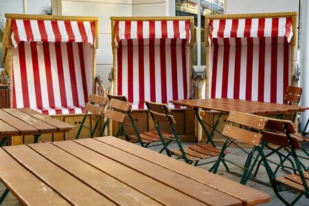 View to a group of wooden patio furniture on the terrace of a restaurant with three beach chairs in the background.の写真素材