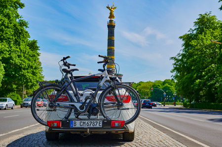 Berlin, Germany - May 8, 2020: Parked car with a bike carrier attached to the stern and bicycles mounted on it. In the background you see the unfocussed Berlin Siegessaeule, a historic landmark.のeditorial素材
