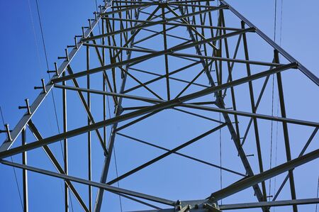 Low angle shot from below to the top of an electricity pylon against blue sky.