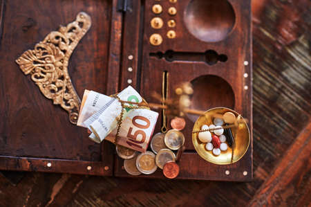 An old scale with money on one side and tablets on the other as a symbol of healthcare costs. The focus lies on the pills and the banknotes.の写真素材