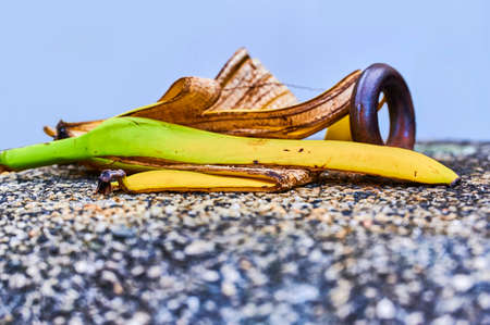 View to a banana peel lying on a concrete bollard with pebbles next to a metal ring.の写真素材