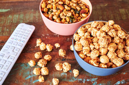 Wooden table with snacks and a TV remote control.の写真素材