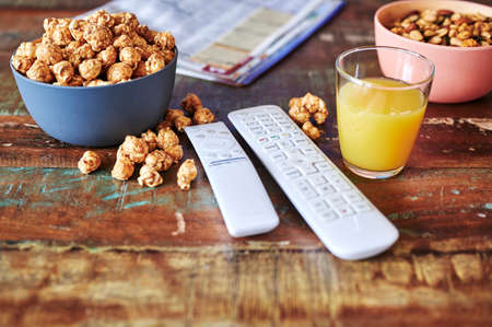 Wooden table with snacks, remote controls and a TV newspaper.の写真素材