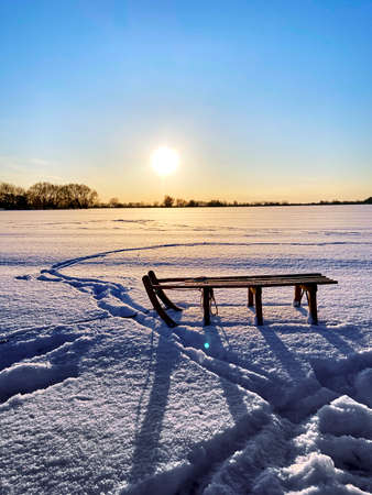 Backlit photo of a sledge standing on a snowy plain in the light of the setting sun.の写真素材