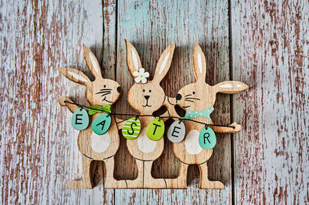 Three wooden Easter bunnies with decoration and the text Easter written on eggs.