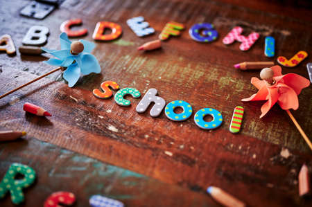 Auburn wooden table with colorful letters that make up the word school and other letters around it.