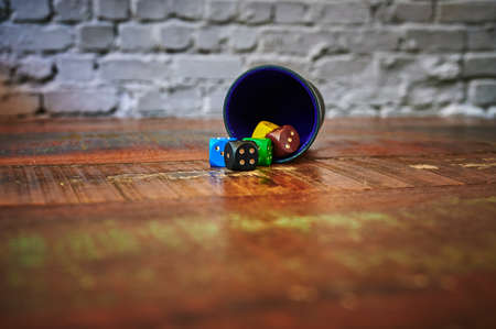 View to different colored game dices and a dice cup on a wooden table.の写真素材
