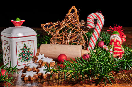 Christmas scene with cinnamon stars, rolling pin, a ceramic biscuit tin and other christmas decoration on an old wooden table.の写真素材