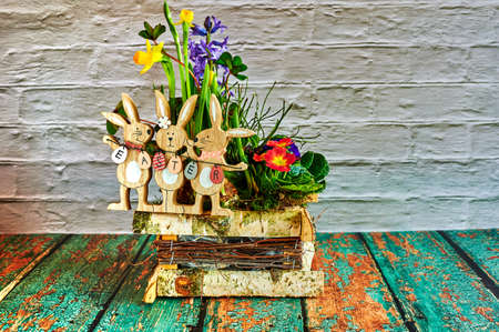 Flower arrangement with wooden Easter bunnies as decoration and the text Easter on the Easter eggs.
