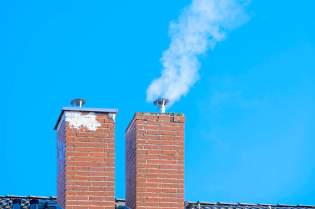 View of two chimneys against a blue sky, the right one is smoking.の写真素材