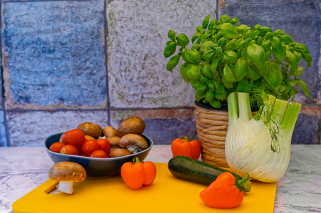 Various raw and fresh vegetable ingredients for cooking in front of a tiled kitchen wall.の写真素材
